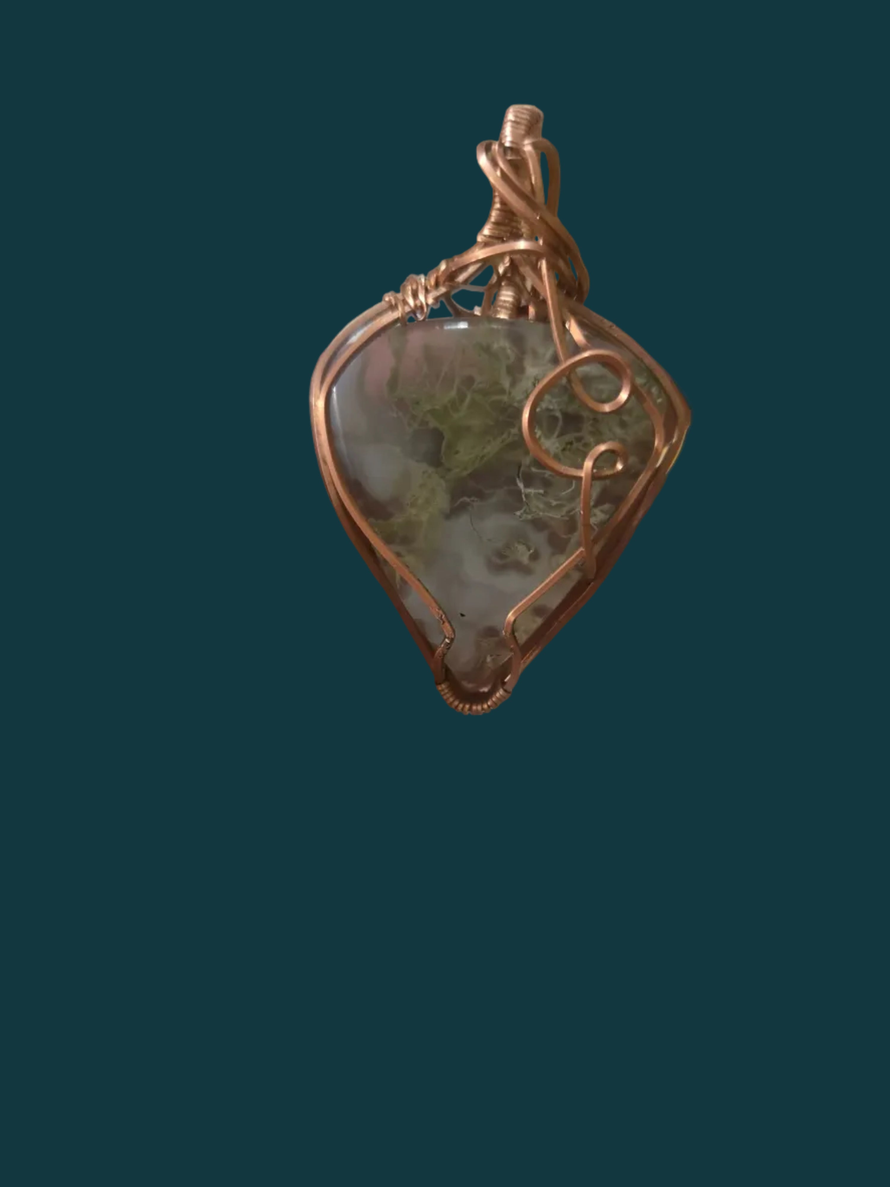 Hand holding a copper-wrapped pendant with a green stone against a blurred background